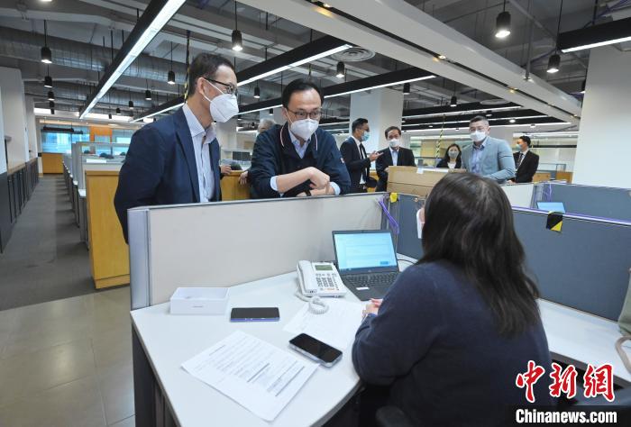 聶德權(quán)(左二)與在電話(huà)熱線(xiàn)中心協(xié)助市民登記“疫苗到戶(hù)接種服務(wù)”的明愛(ài)專(zhuān)上學(xué)院學(xué)生交談。　香港特區(qū)政府新聞處供圖