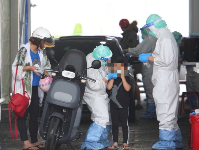 本土疫情升溫，一位家長帶著小孩騎車前往排隊(duì)篩檢。（張鎧乙攝）