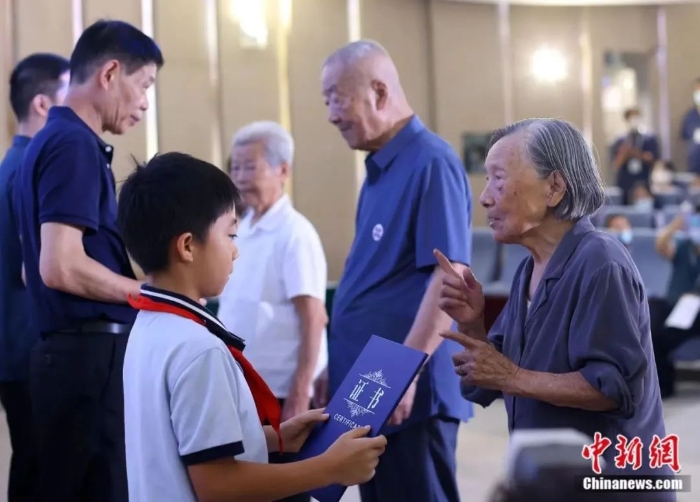 圖片南京大屠殺幸存者夏淑琴(右一)、葛道榮(右二)、艾義英(右三)向南京大屠殺幸存者后代代表頒發(fā)“南京大屠殺歷史記憶傳承人”證書。泱波 攝