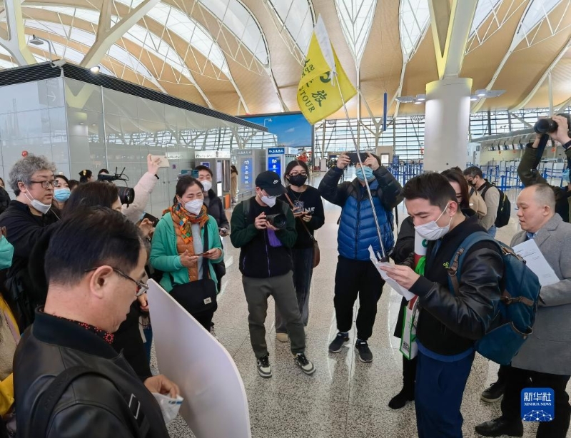 2月6日，在上海浦東國際機(jī)場(chǎng)，出境團(tuán)隊(duì)游領(lǐng)隊(duì)師文（舉旗者）向游客說明相關(guān)注意事項(xiàng)。（圖源：新華社）