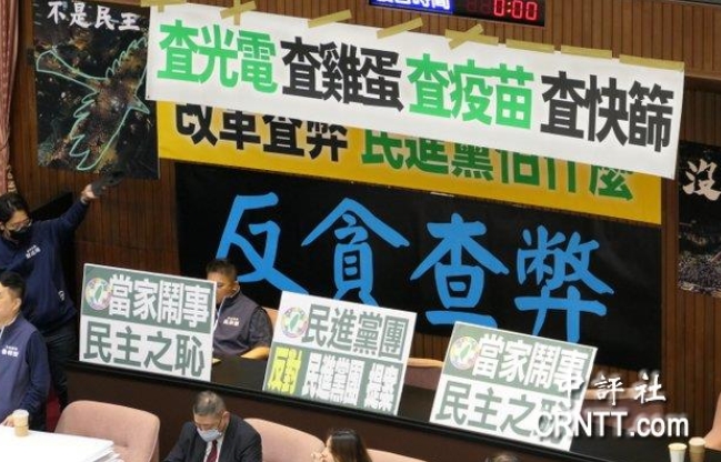 “立院”議場(chǎng)內(nèi)貼滿藍(lán)綠白的布條海報(bào)，上面寫(xiě)著“查光電、查疫苗、查快篩”等字